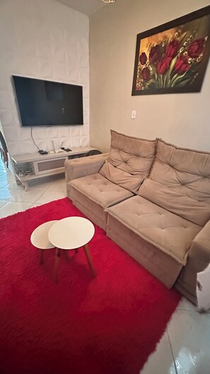 A living room with a beige sofa, a red rug, a white coffee table, and a flat-screen TV mounted on the wall.