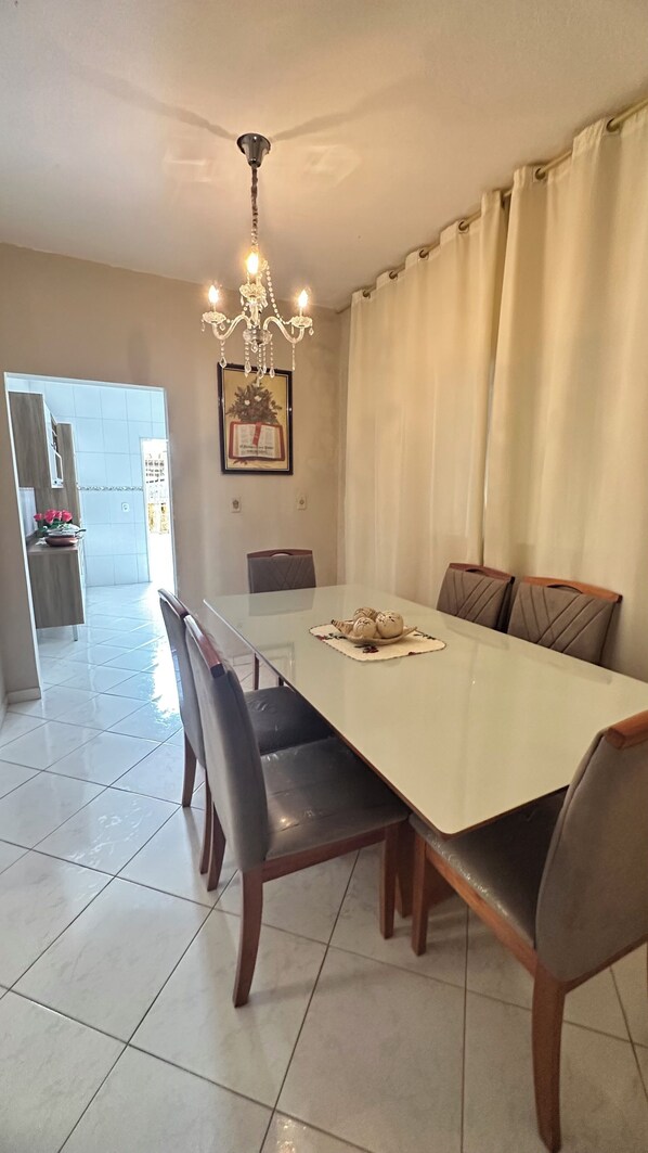 A dining area with a long table, chairs, a chandelier, and a view into another room.