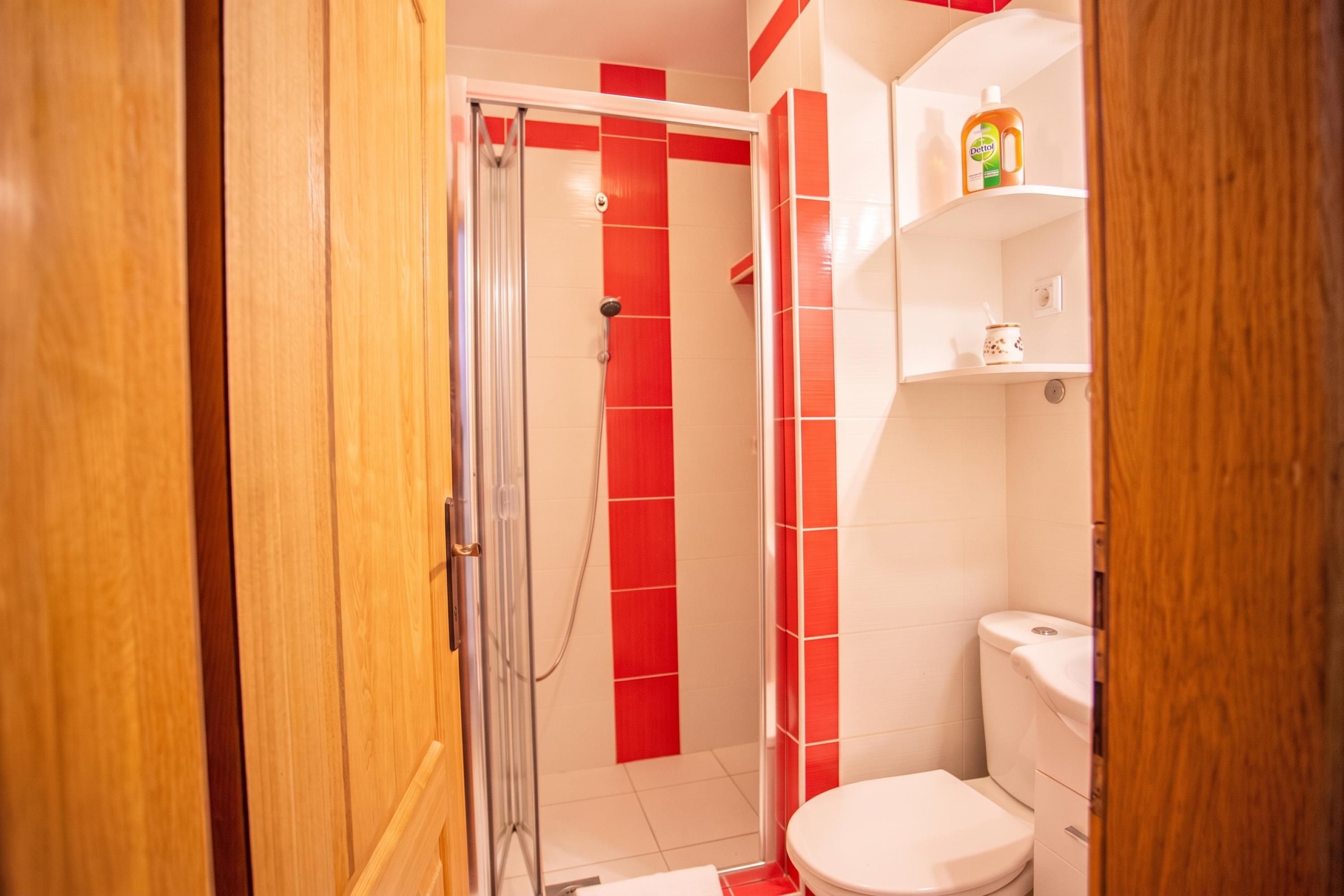 Un baño con ducha, inodoro y repisa con artículos de aseo.