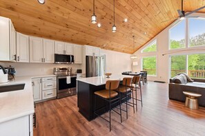 A spacious kitchen with wooden ceiling, white cabinets, stainless steel appliances, and a bar area with stools.