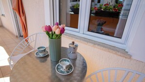 A round table with a vase of tulips, two cups, and a coffee maker on a balcony with white chairs and a view of buildings and plants. - Lovely Studio Apartment 4 Vrsar, Vrsar, Croatia (Vrsar)