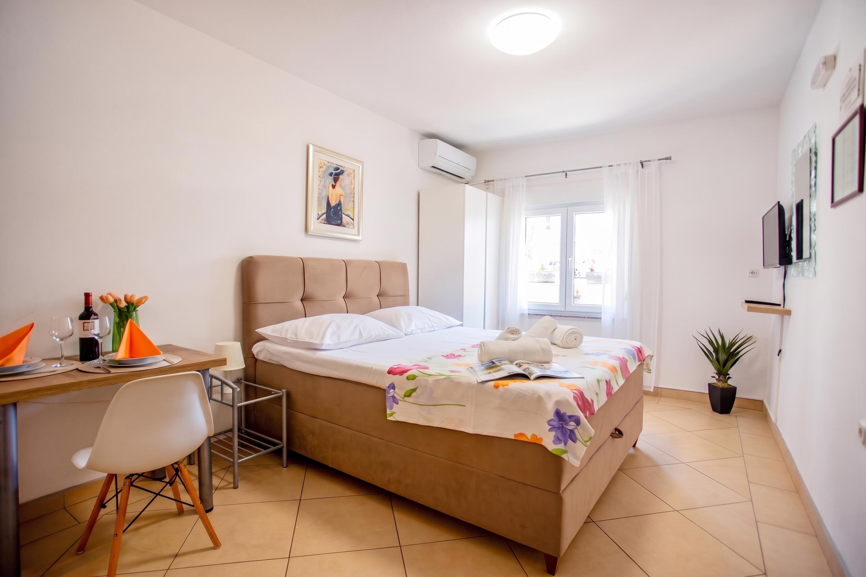 Une chambre d’hôtel avec un lit, un bureau, une chaise, une plante en pot et une fenêtre avec des rideaux.