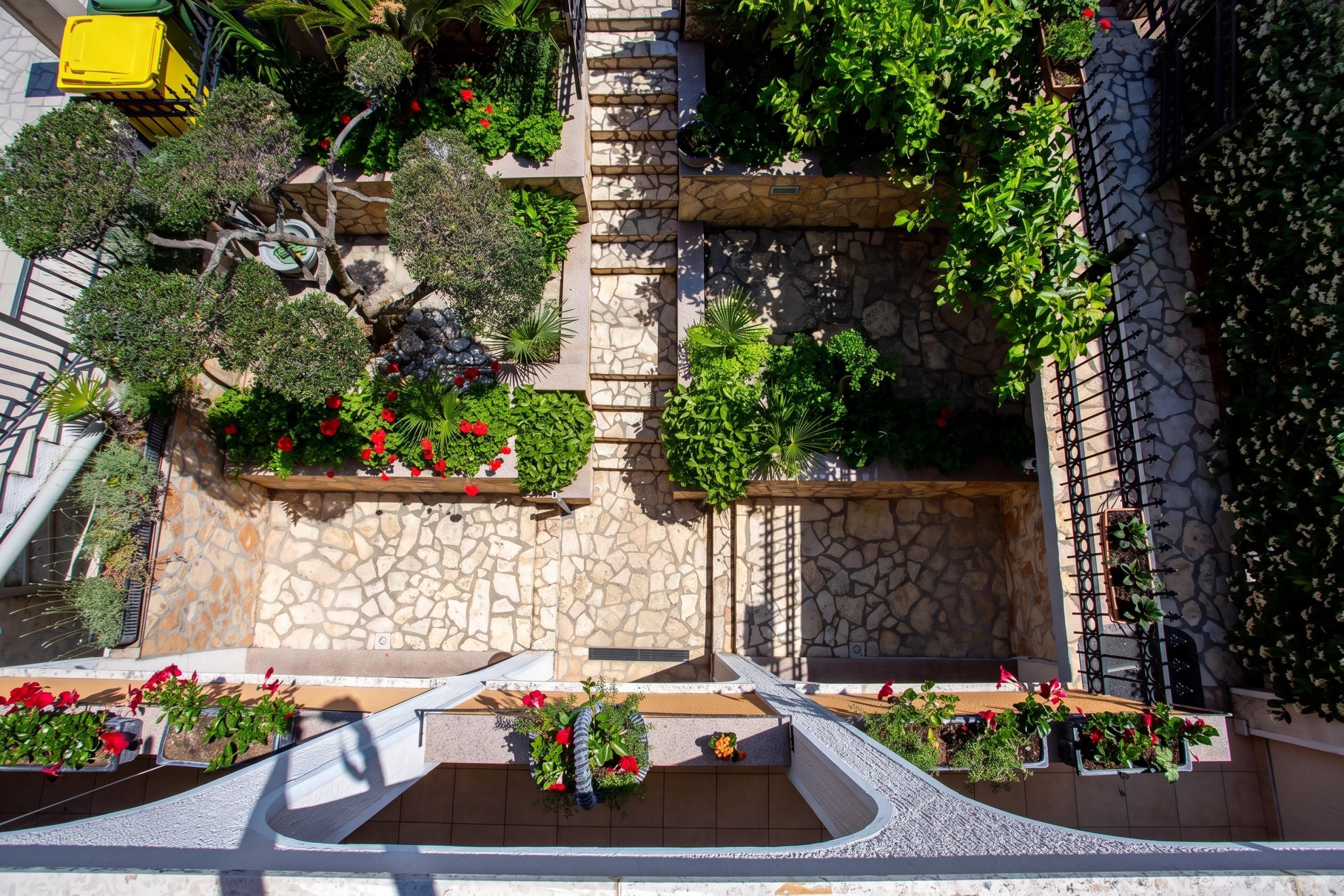 A rooftop garden with stone walls, various plants, and a seating area.