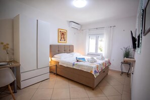 Een slaapkamer met een bed, een bureau, een stoel, een raam met gordijnen en een wandairconditioner.