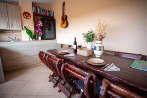 A dining area with a wooden table set for four, surrounded by chairs. A guitar hangs on the wall, and there are books and a green bottle on a shelf. - Lovely Studio Apartment 5 Vrsar, Vrsar, Croatia (Vrsar)