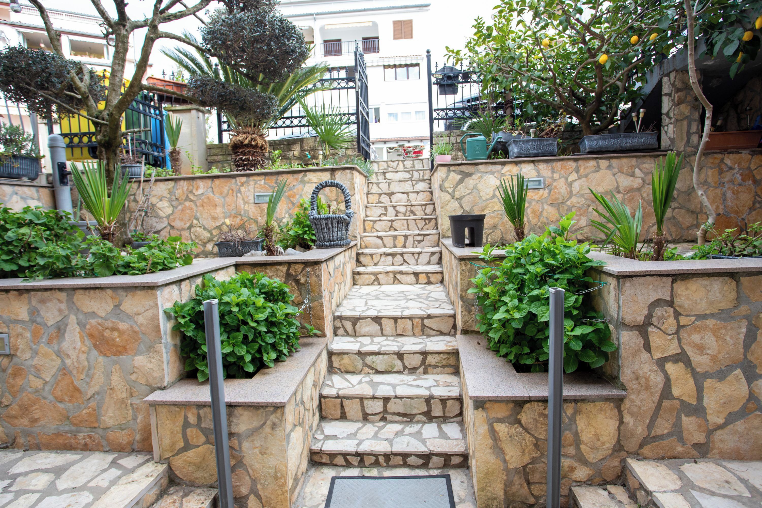 Un escalier en pierre mène à un jardin sur le toit, où l’on trouve des plantes en pot, et d’où l’on peut admirer les bâtiments qui se dressent à l’horizon.