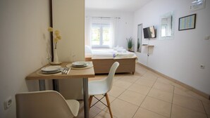 A hotel room with a bed, a desk with a chair, a small table with a vase of flowers, and a television on the wall. - Lovely Studio Apartment 5 Vrsar, Vrsar, Croatia (Vrsar)