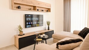A modern living room with a flat-screen TV, wooden shelves, a small table with a plant, and a sofa. - Viviani Court 2bd Modern Apt Xewkija Gozo, XEWKIJA Gozo, Malta (XEWKIJA Gozo)