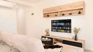 A modern living room with a sofa, a coffee table, a TV mounted on the wall, and a wooden shelf above. - Viviani Court 2bd Modern Apt Xewkija Gozo, XEWKIJA Gozo, Malta (XEWKIJA Gozo)