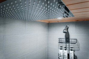 Une douche avec un pommeau de douche en forme de pluie, une étagère en métal avec des bouteilles et un plafond en bois.