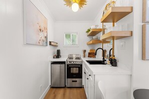 Cocina pequeña con lavavajillas, estufa, horno y muebles blancos.