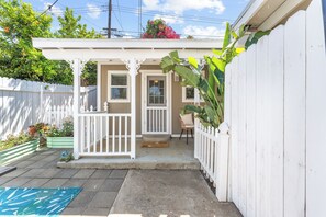 A small house with a porch, a white fence, and a garden with plants and flowers. - Welcome to this cozy, stylish escape- private guesthouse in beautiful Redlands (Redlands)