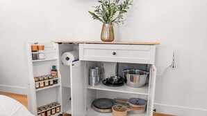 Un meuble de cuisine blanc avec un plan de travail en bois, un vase contenant des feuilles vertes, ainsi que divers ustensiles et récipients de cuisine.