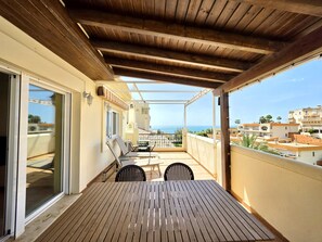 A wooden balcony with a table and chairs, a glass door, and a view of the sea and buildings. - SR Torrequebrada 1 BDR with sea view (Benalmadena Costa)