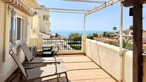Uma varanda com vista para o mar, uma mesa com cadeiras e uma estrutura de pérgula.