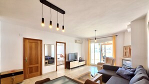 Uma sala de estar moderna com sofá, mesa de centro, televisão e porta de vidro deslizante para uma varanda.