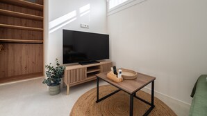 Een moderne woonkamer met een flatscreen-tv, houten planken, een klein tafeltje en een plant in pot.