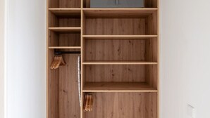 Een inloopkast met houten planken, een grijze opbergkist en een kledingroede.
