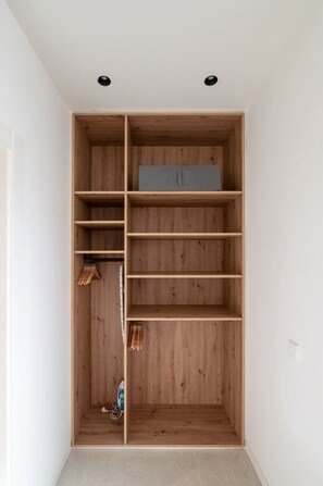 A walk-in closet with wooden shelving, a gray storage box, and hanging space. - GuestReady - Super cozy studio in Madrid (Madrid)