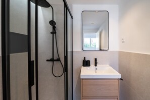 A modern bathroom with a glass shower enclosure, a white sink, a wooden cabinet, and a mirror above the sink. - GuestReady - Estudio super acogedor en Madrid (Madrid)