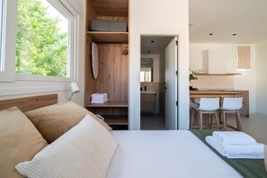A bedroom with a bed, a bedside lamp, a view of the outdoors, a bathroom with a mirror, and a kitchen area with chairs. - GuestReady - Estudio super acogedor en Madrid (Madrid)