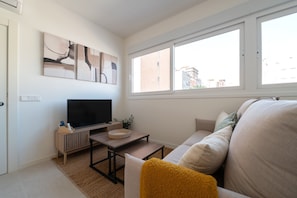 A living room with a TV, a small table, a sofa, and a window with a view of buildings. - GuestReady - Estudio super acogedor en Madrid (Madrid)