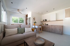 A modern living room with a sofa, a coffee table, and a kitchen area with wooden cabinets and a microwave. - GuestReady - Estudio super acogedor en Madrid (Madrid)