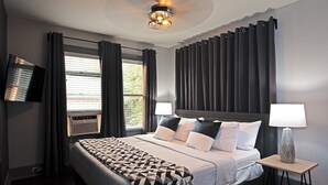 Habitación de hotel con una cama, dos lámparas de noche, un televisor y una ventana con cortinas.