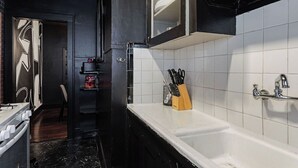Una cocina estrecha con encimera blanca, un lavamanos y un armario negro con puerta de cristal.