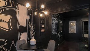 Una habitación moderna con una mesa redonda, dos sillas, un jarrón con flores y una pared decorada con diseños abstractos y un reloj.