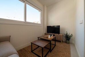 Ein Zimmer mit Fernseher, kleinem Tisch, einer Couch und einem Fenster.