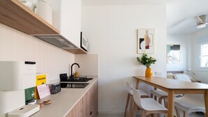 Moderni keittiö, jossa on sisäänrakennettu liesi, pesuallas sekä ruokailutila, jossa on puinen pöytä ja valkoiset tuolit.