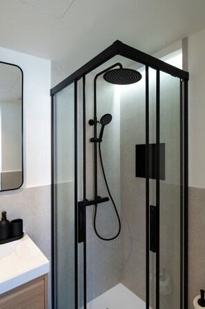 Ein modernes Badezimmer mit einer Duschkabine aus Glas, einem weißen Waschbecken und einem Spiegel.