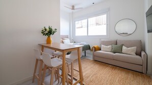 A modern living room with a dining area, a sofa, a mirror, and a window.