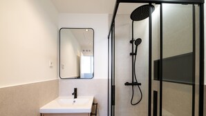A bathroom with a white sink, a mirror, a shower with a black handheld showerhead, and a glass-enclosed shower area.