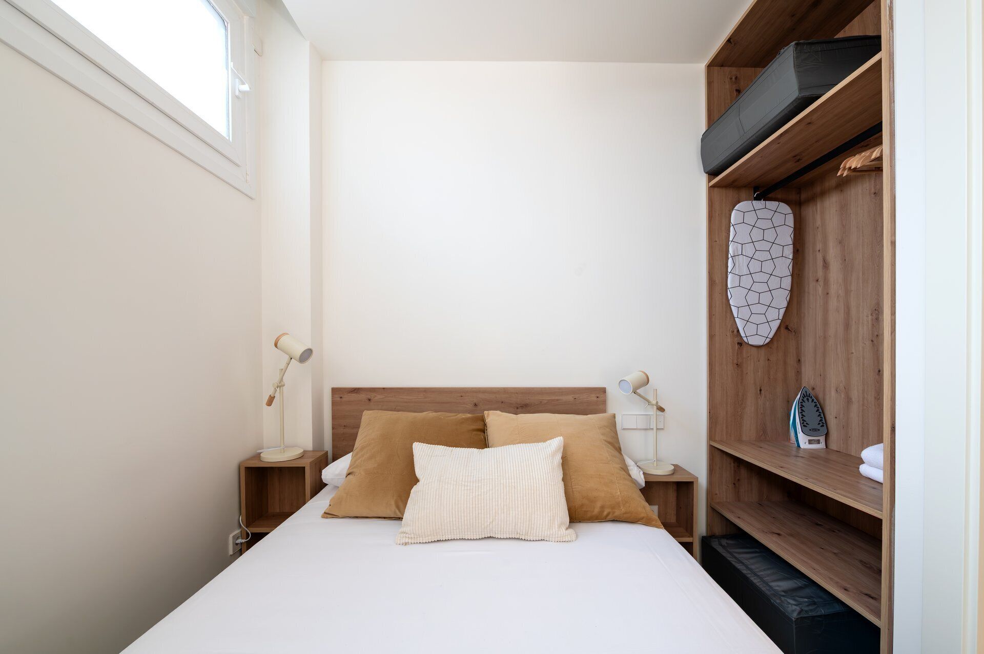 Un dormitorio con cabecera de madera, dos mesitas de noche con lámparas, cama con dos almohadas y estante con una tabla de surf y una toalla.