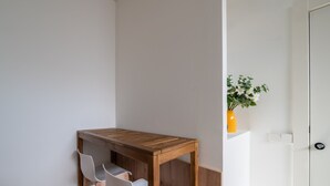 Een hoekkamer met een houten tafel en twee witte stoelen, een witte deur, en een vaas met bloemen op een witte plank.