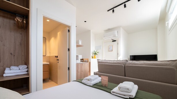 Een hotelkamer met een bed, een slaapbank, een houten garderobe, een badkamer en een televisie.