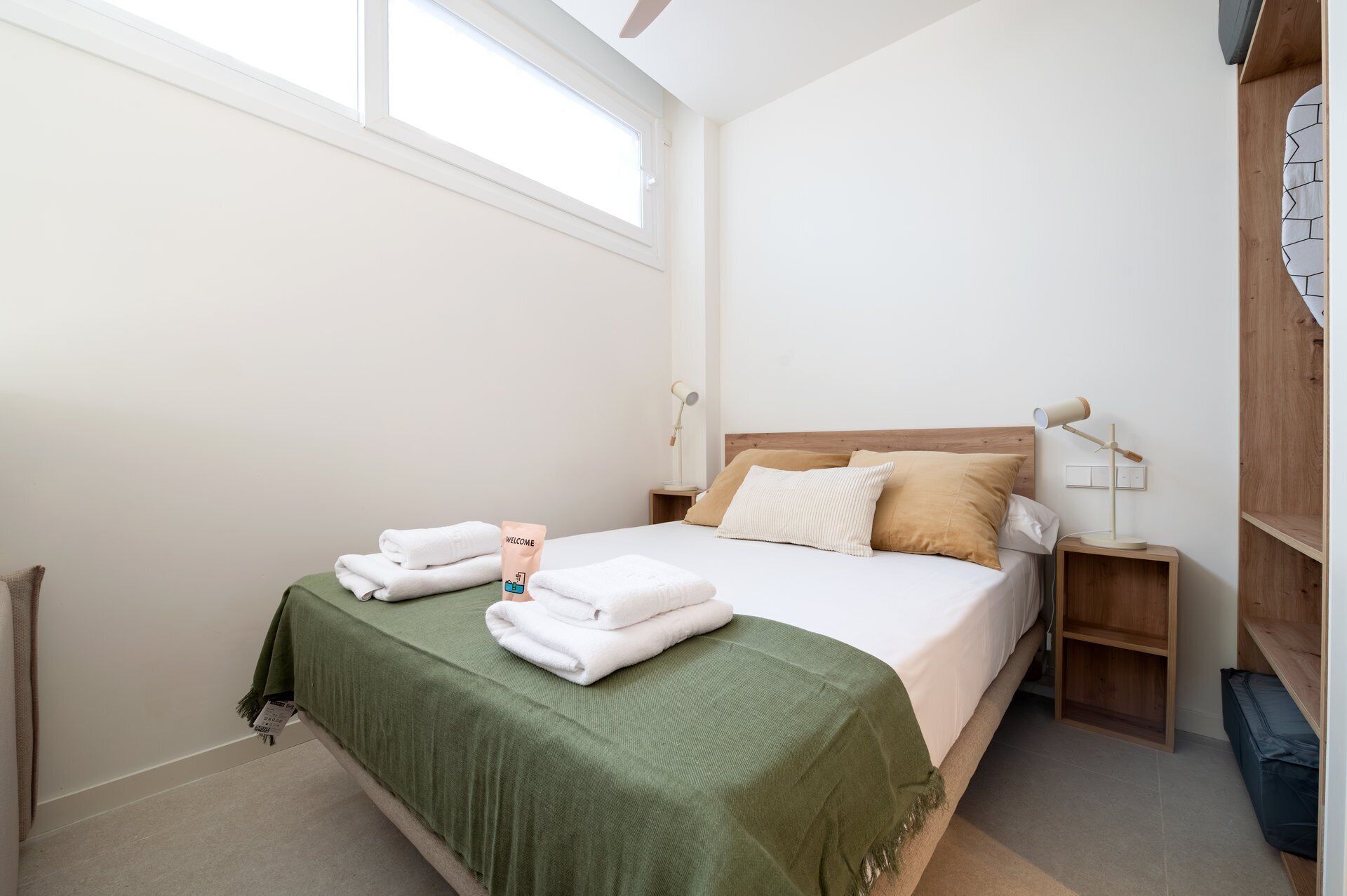 A neatly made bed with a green bedspread, two pillows, and a bedside lamp.