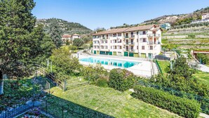 A hotel with a swimming pool, surrounded by greenery and hills.