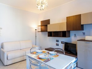 A modern living space with a white sofa, a dining table set with plates and glasses, a flat-screen TV, and wooden cabinets.