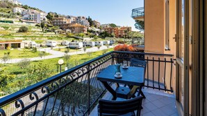 A balcony with a table and chairs, overlooking a residential area with houses and parked vehicles.