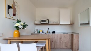 Eine kleine Küche mit Mikrowelle, Spüle und Holzschränken. Ein Esstisch mit zwei Stühlen und eine Vase mit Blumen stehen links.
