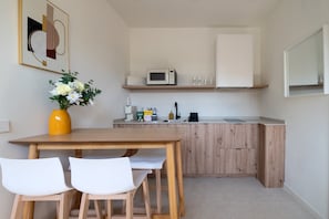 A compact kitchen with a microwave, sink, and wooden cabinets. There is a dining table with two chairs and a vase with flowers on the left. - GuestReady - Estudio super acogedor en Madrid (Madrid)
