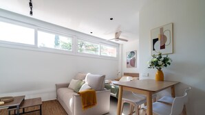 Ein modernes Wohnzimmer mit einer Couch, einem Esstisch mit Stühlen, einem Deckenventilator und Kunstwerken an der Wand.
