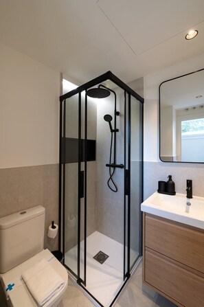 A modern bathroom with a glass-enclosed shower, a white toilet, a wooden vanity with a mirror, and a white sink. - GuestReady - Estudio super acogedor en Madrid (Madrid)