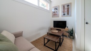 Un salón con un sofá, un televisor sobre un mueble de madera, una mesita y dos cuadros abstractos en la pared.