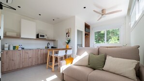 Una cocina moderna con armarios blancos, una zona de comedor con una mesa y sillas, y una sala de estar con un sofá y un ventilador de techo.