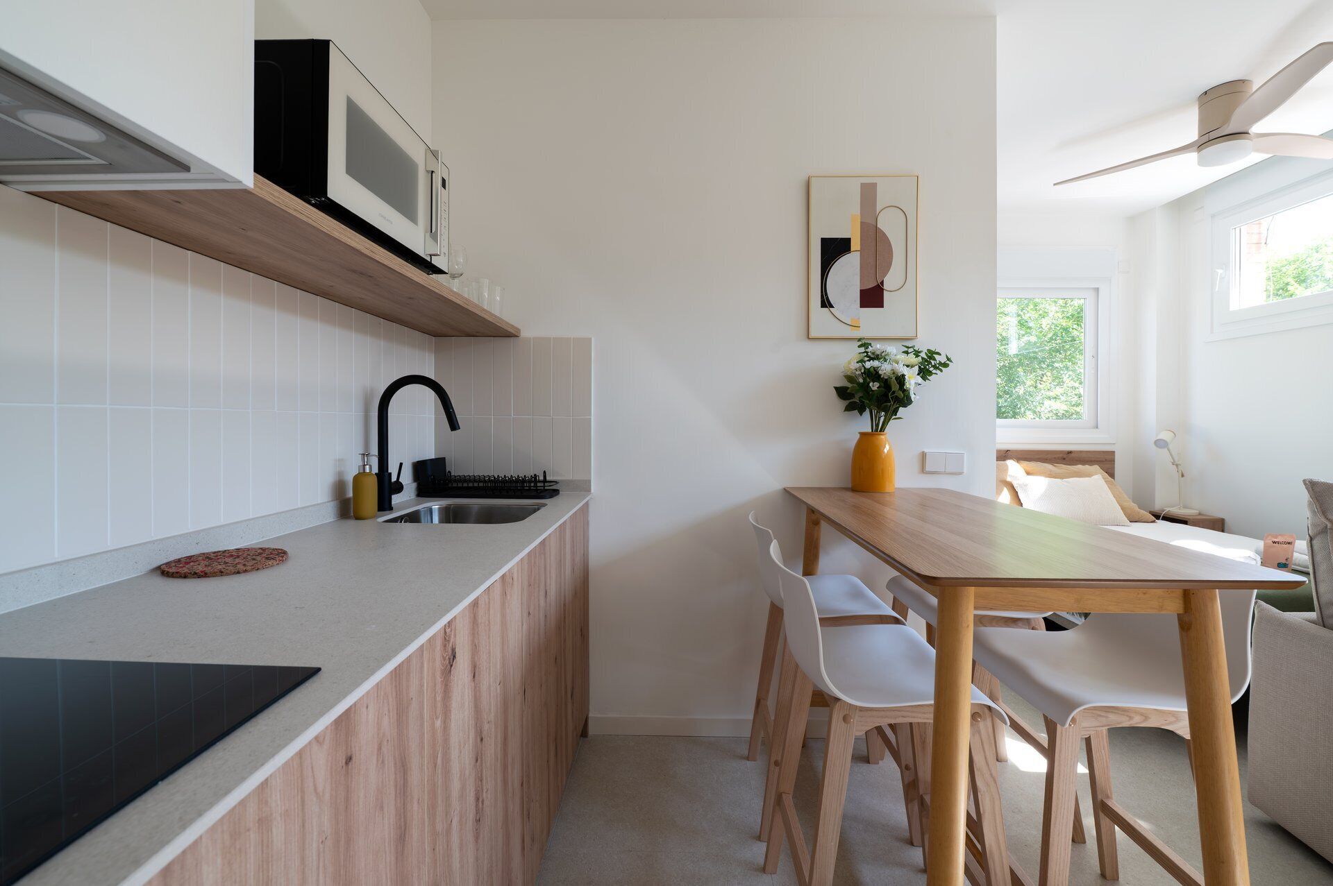Une cuisine moderne équipée d’un four à micro-ondes encastré, d’un évier et d’un coin repas avec une table en bois et des chaises blanches.