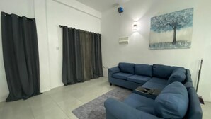 Un salon avec un canapé bleu, un tapis gris et un tableau représentant un arbre accroché au mur.